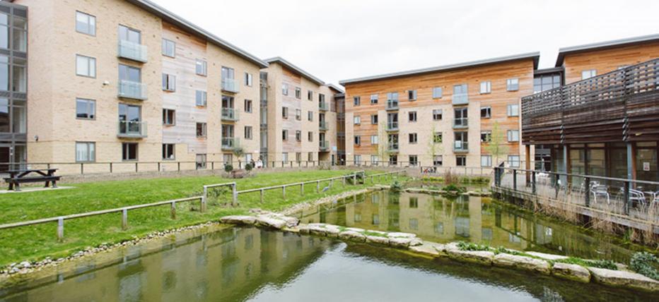 Modern four story accommodation blocks surrounding a lake and grass areas.