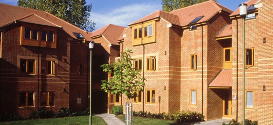 Brown brick accommodation blocks with lovely grass areas and paved footpaths. Blue skies and trees peeping over the buildings.