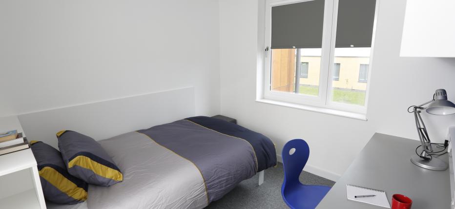 Interior shot of enhanced ensuite room, with a small double bed, wardrobe, work desk and swivel chair