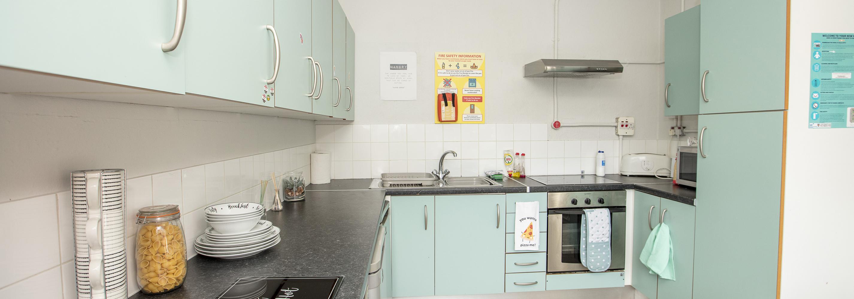Kitchenm extractor fan, teal coloured cupboards, oven, hob, sink, toaster, fire blanket