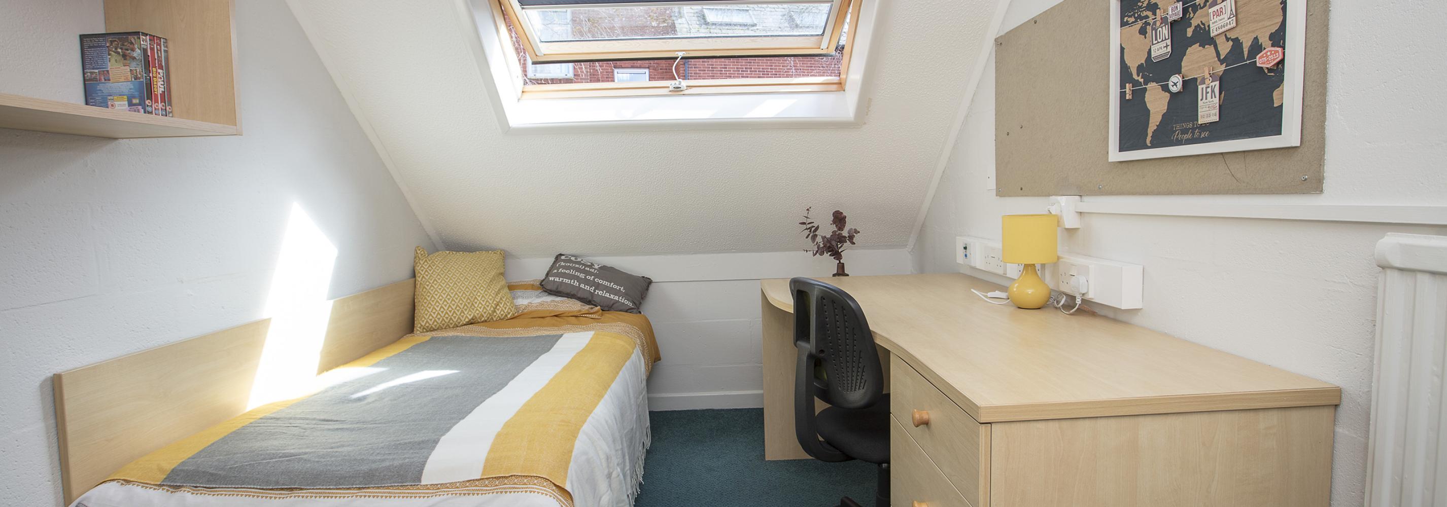 Loft room, single bed, desk, chair, noticeboard, shelves, overhead window, radiator