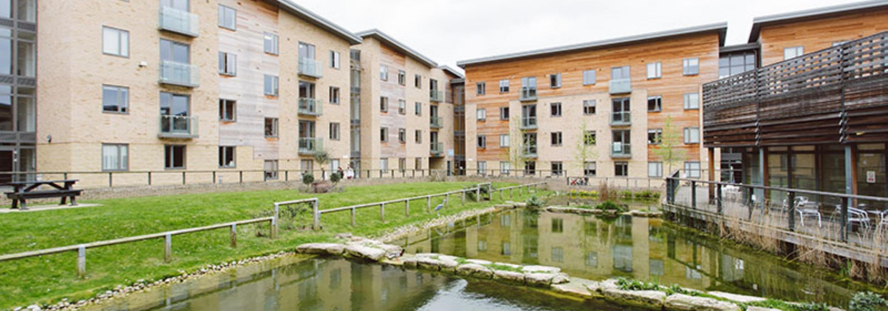 Modern four story accommodation blocks surrounding a lake and grass areas.