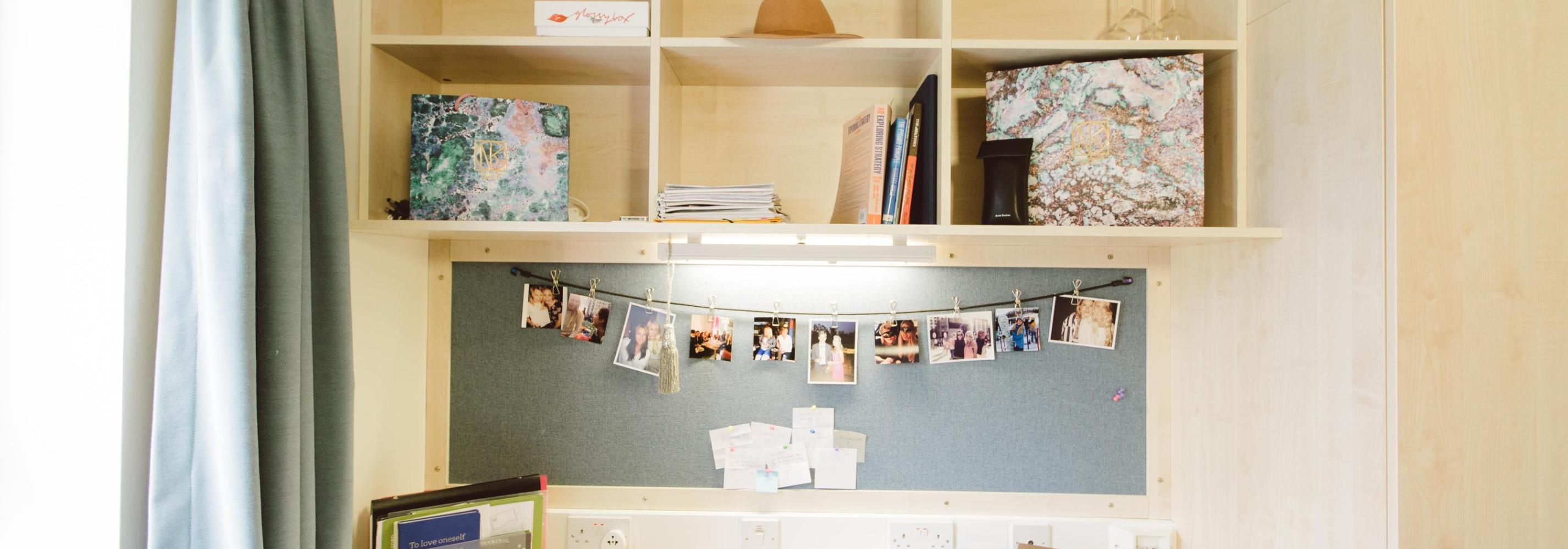 Built in wooden desk and shelving. Pin board with photos on the wall.