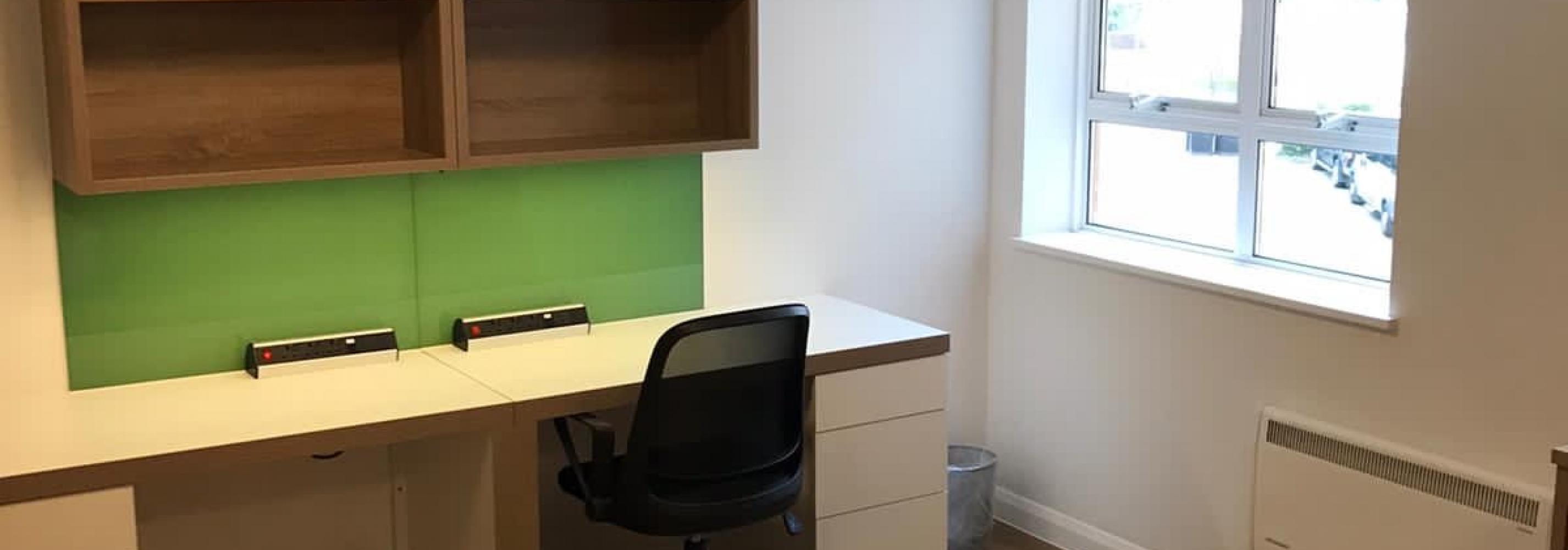 Double desk with shelving above. Window to the right. One desk chair tucked in.