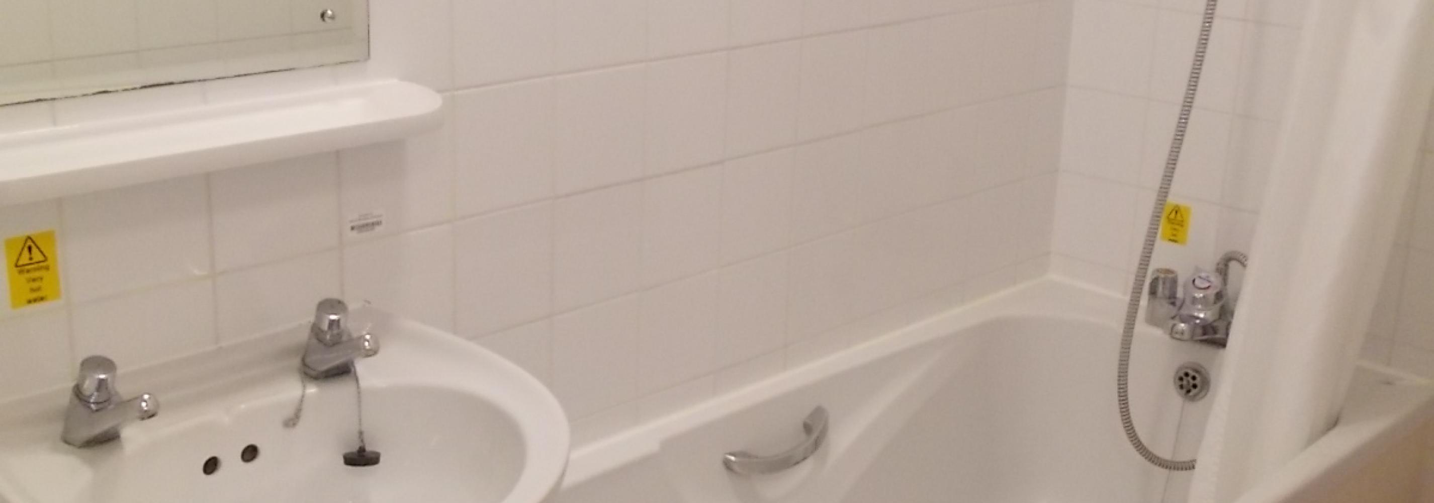 Full white bathroom with toilet, basin, mirror, bath and in-bath shower.