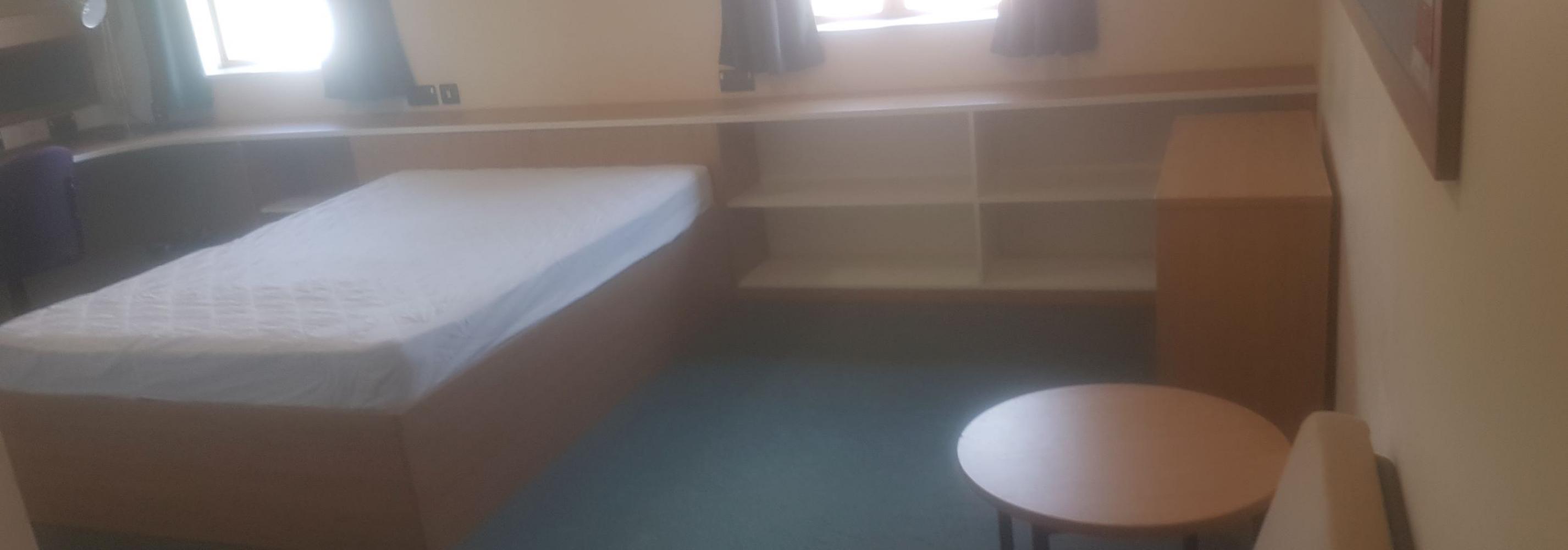 Large double room with double bed, chair, storage, coffee table and two windows.