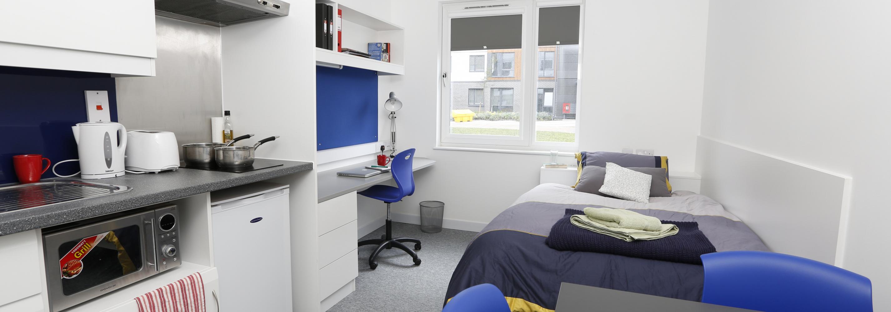 Interior shot of a studio flat, with a small double bed, work/study area, ensuite bathroom and kitchen area