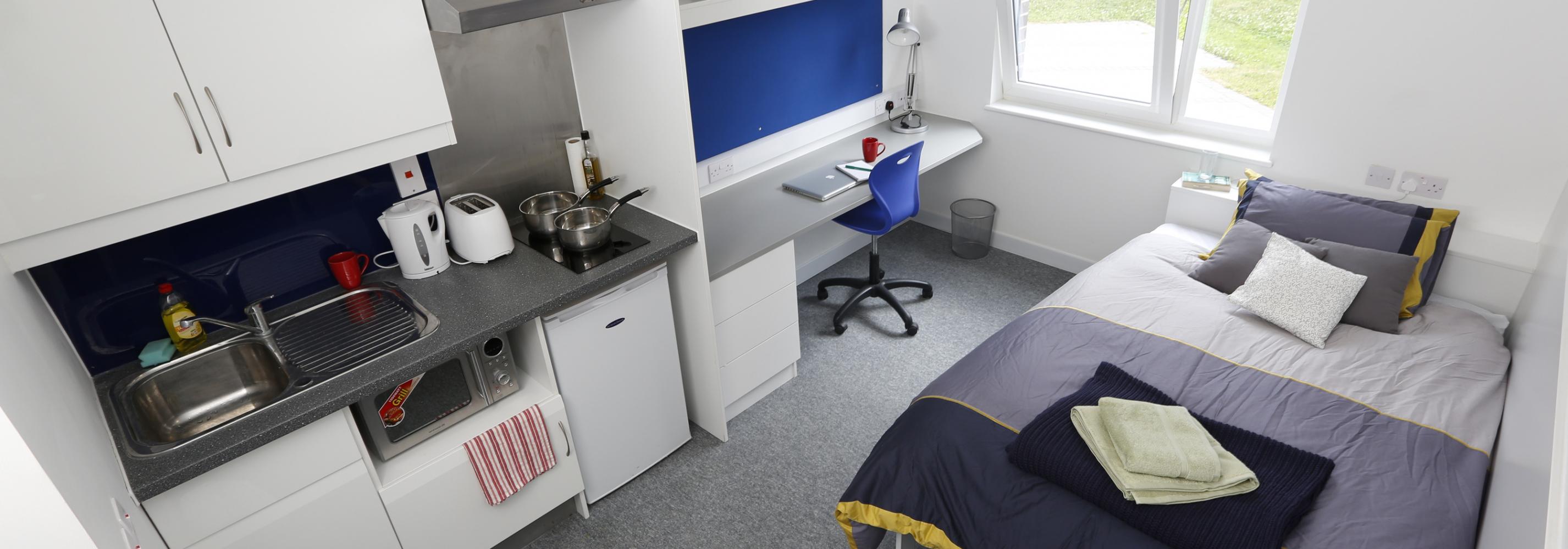 Interior shot of a studio flat, with a small double bed, work/study area, ensuite bathroom and kitchen area