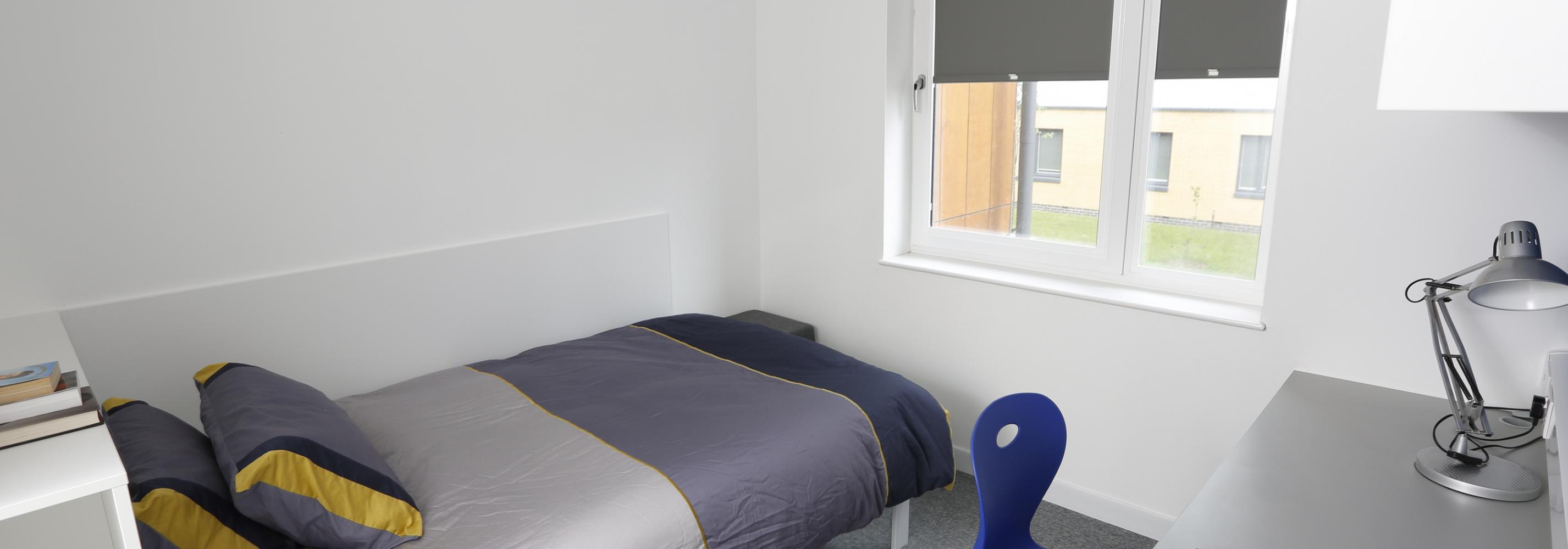 Interior shot of enhanced ensuite room, with a small double bed, wardrobe, work desk and swivel chair