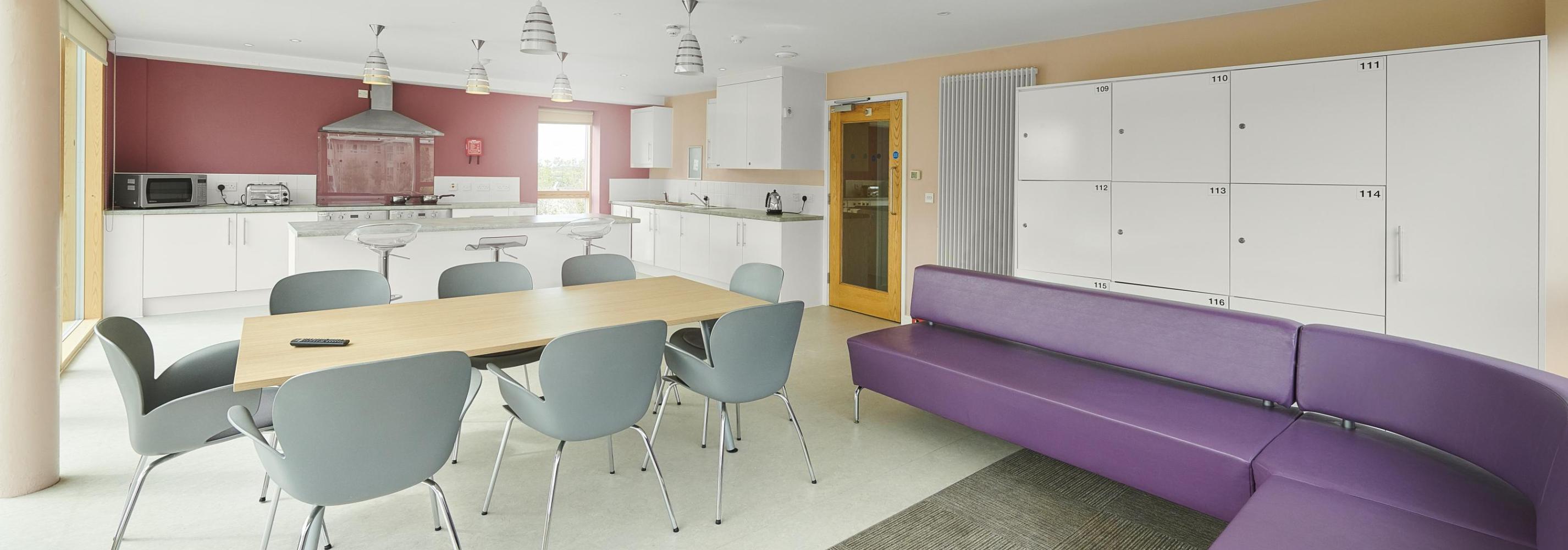 Interior of shared kitchen and dining facilities showing dining table and chairs, sofa seating area and food preparation area. 