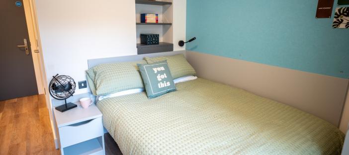 Modern bedroom. Blue and Green theme. Double bed, bedside table and behind the bed shelving.